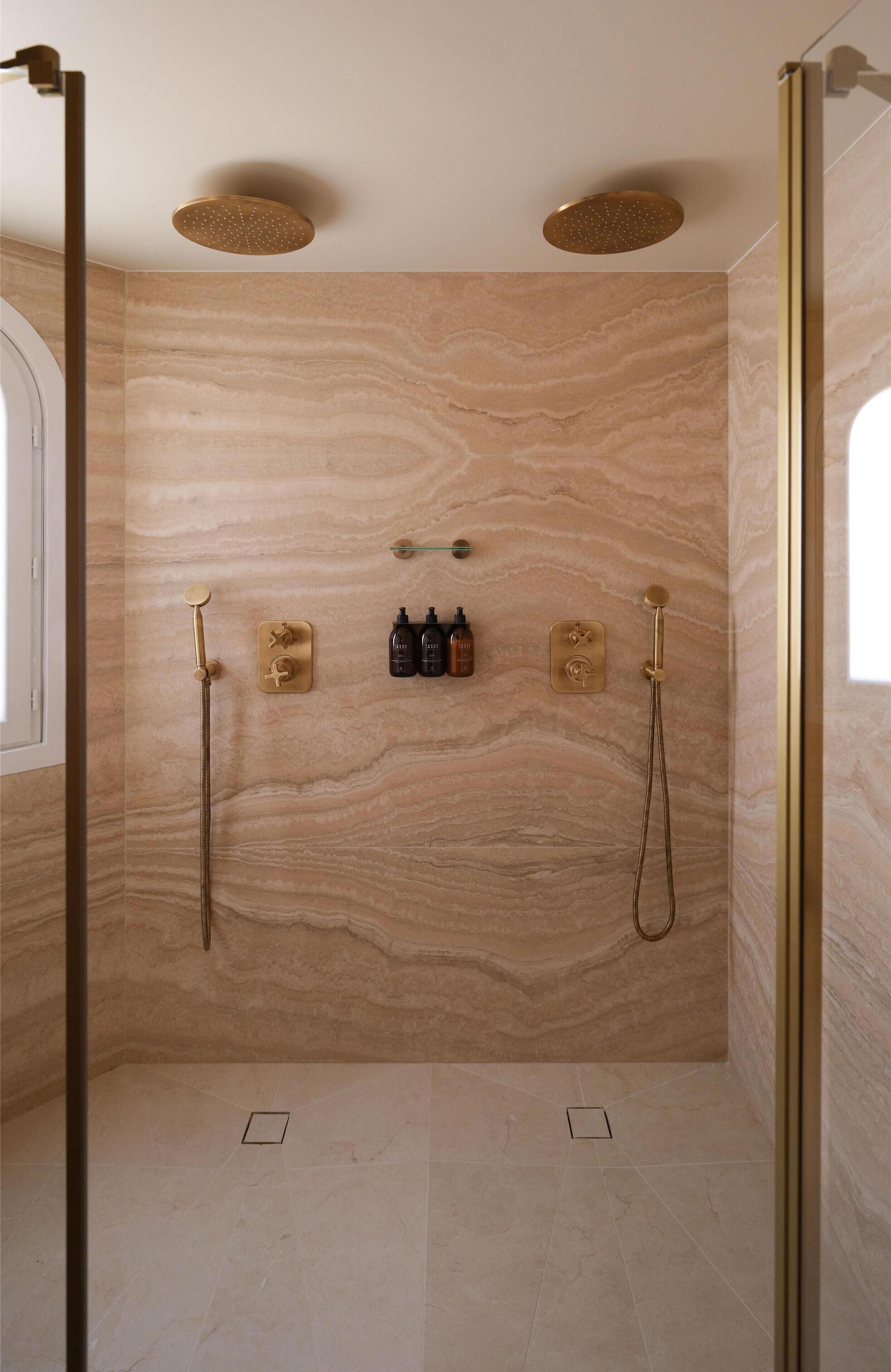 Un baño con paredes de mármol, ducha y tocador con artículos de aseo.
