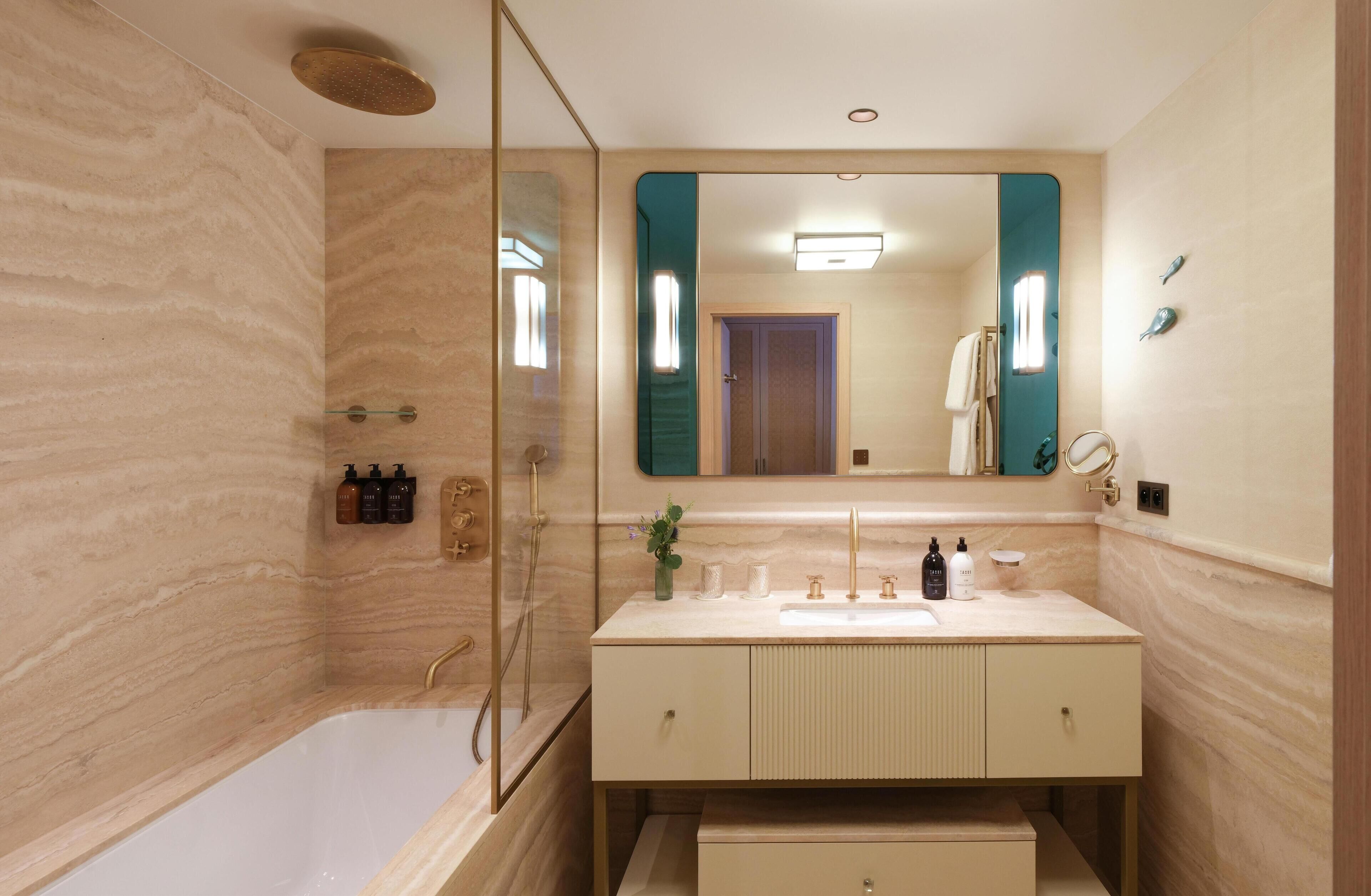 Ein modernes Badezimmer mit Marmorwand, einem großen Spiegel, einer Badewanne und einem Waschtisch mit Pflegeprodukten.