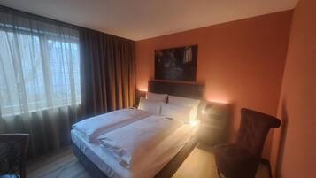 A hotel room with a bed, a chair, a desk, and a painting on the wall.