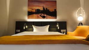 A hotel room with a bed, a cityscape painting, a nightstand, a lamp, and a chair. - Turm Hotel (Frankfurt)