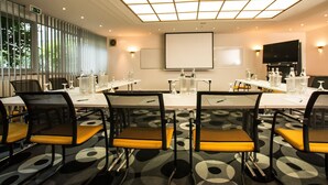 A conference room with a long table, chairs, a projector screen, and a large window with blinds. - Turm Hotel (Frankfurt)