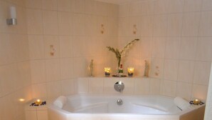 Un baño con una bañera grande, una silla de madera con toallas y objetos decorativos en el suelo.