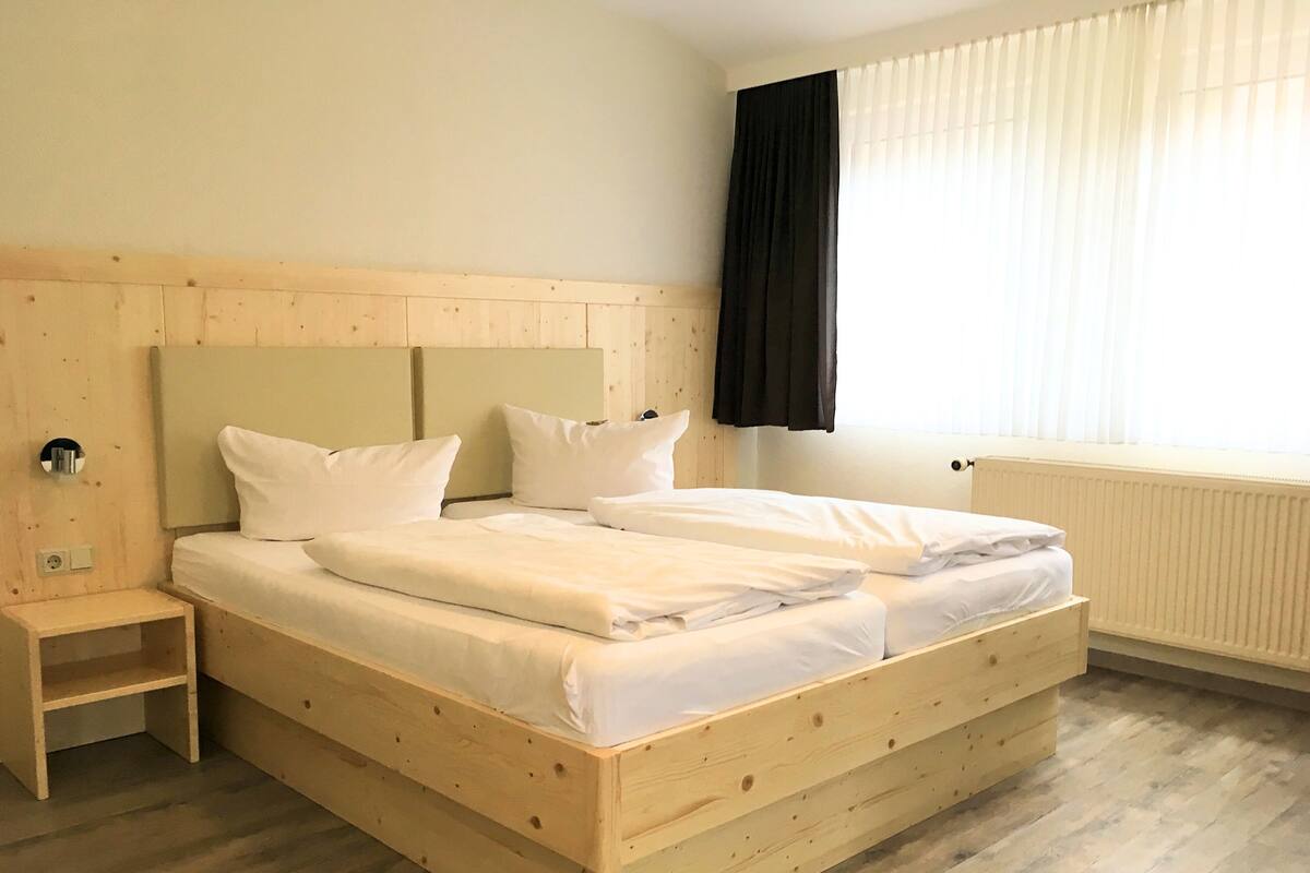 Ein Doppelbett mit Holz Kopfteil, ein Nachttisch und ein Fenster mit Jalousien.