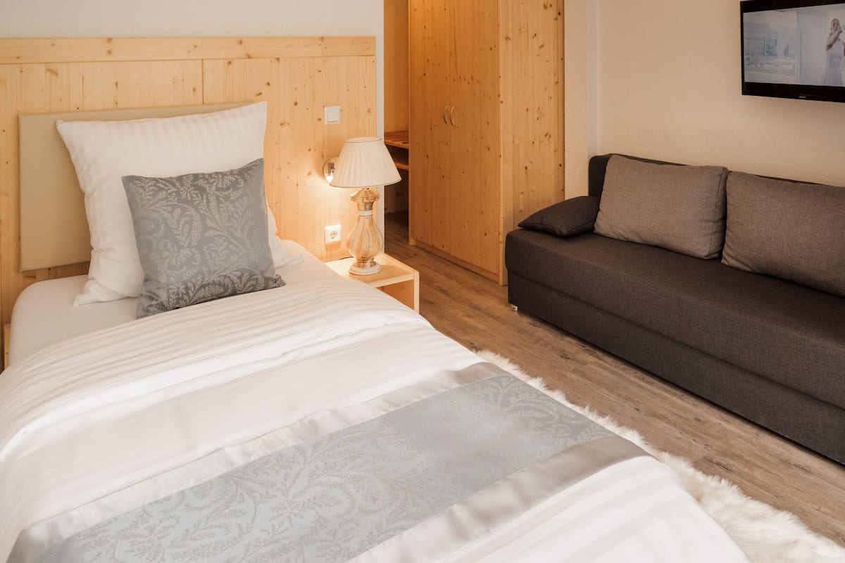 Ein Schlafzimmer mit Bett, Nachttisch, Lampe, Sofa und einem Holzschrank.