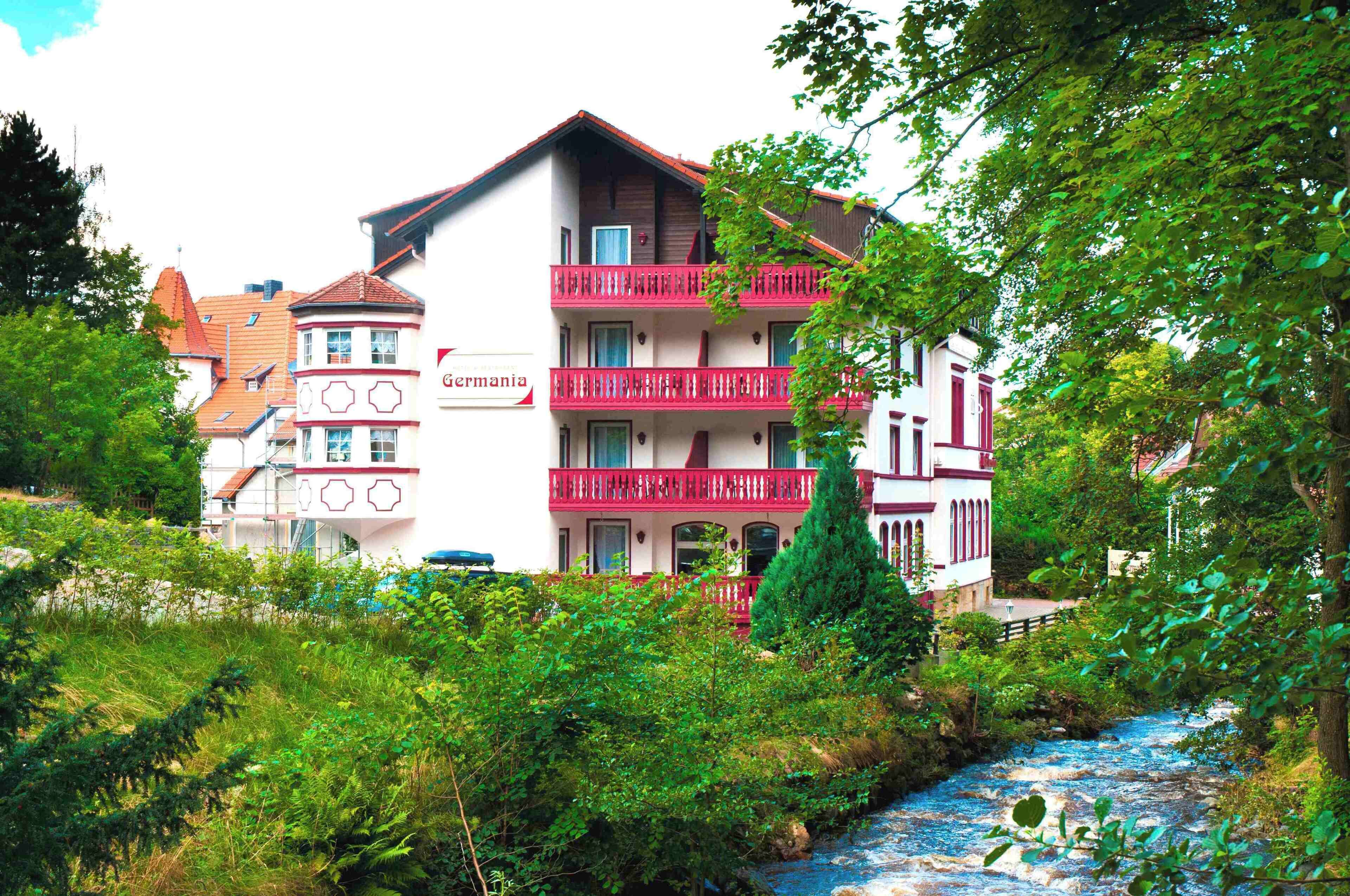 Ein mehrgeschossiges Gebäude mit Balkonen, einem Schild mit der Aufschrift 'Germanyia' und einem Fluss im Vordergrund.