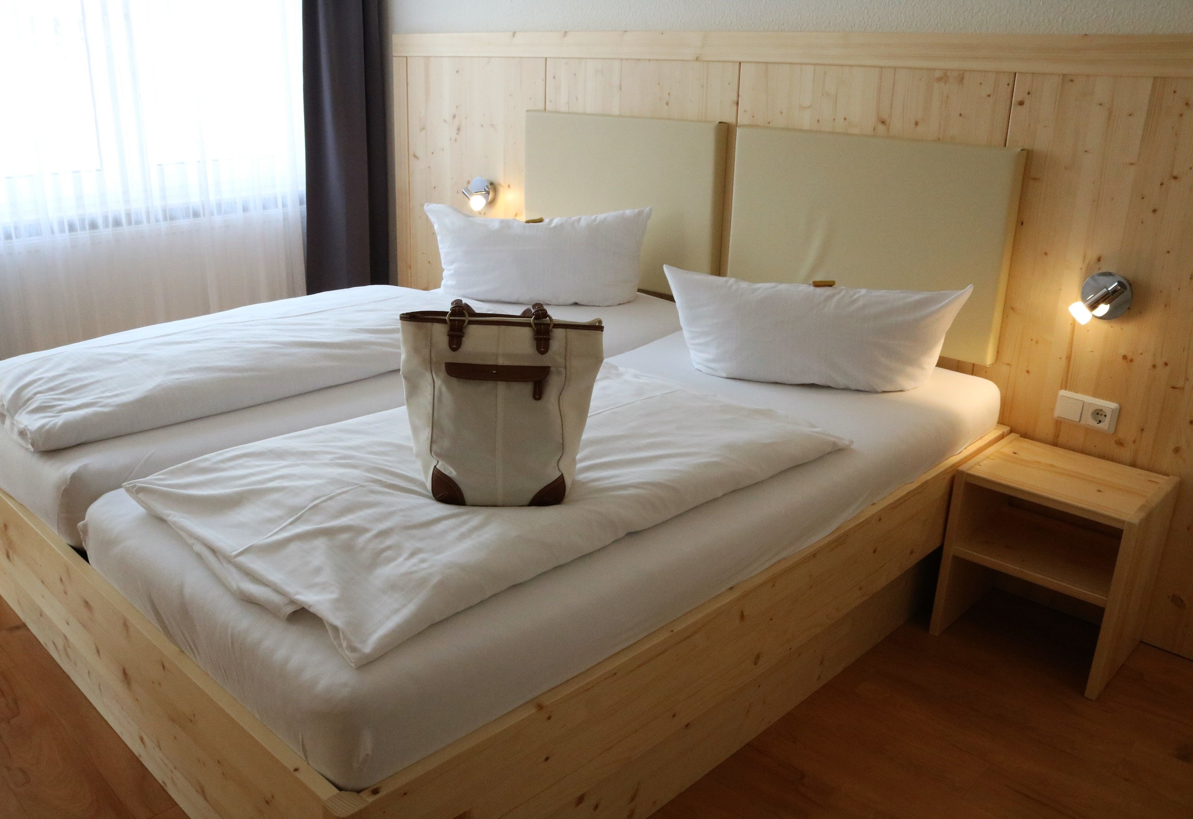 A wooden bed with white linens and pillows, a bedside table with a lamp, and a wooden nightstand.