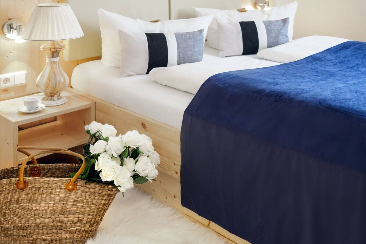 Ein ordentlich eingerichtetes Schlafzimmer mit Bett, Nachttisch, Lampe und einem Korb mit weißen Blumen.