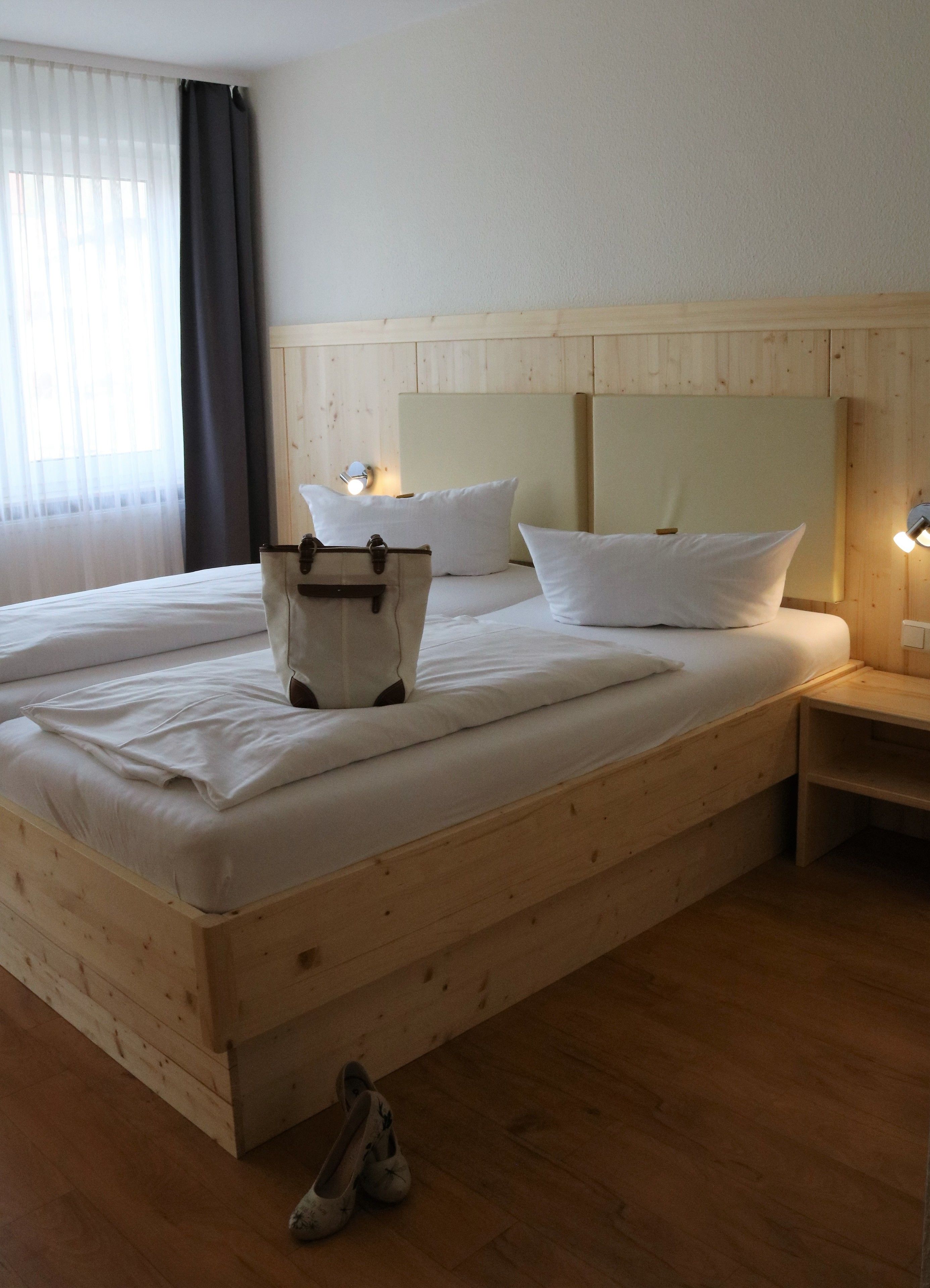 Un lit en bois avec du linge de lit blanc, une table de chevet et une paire de chaussons posés sur le sol.