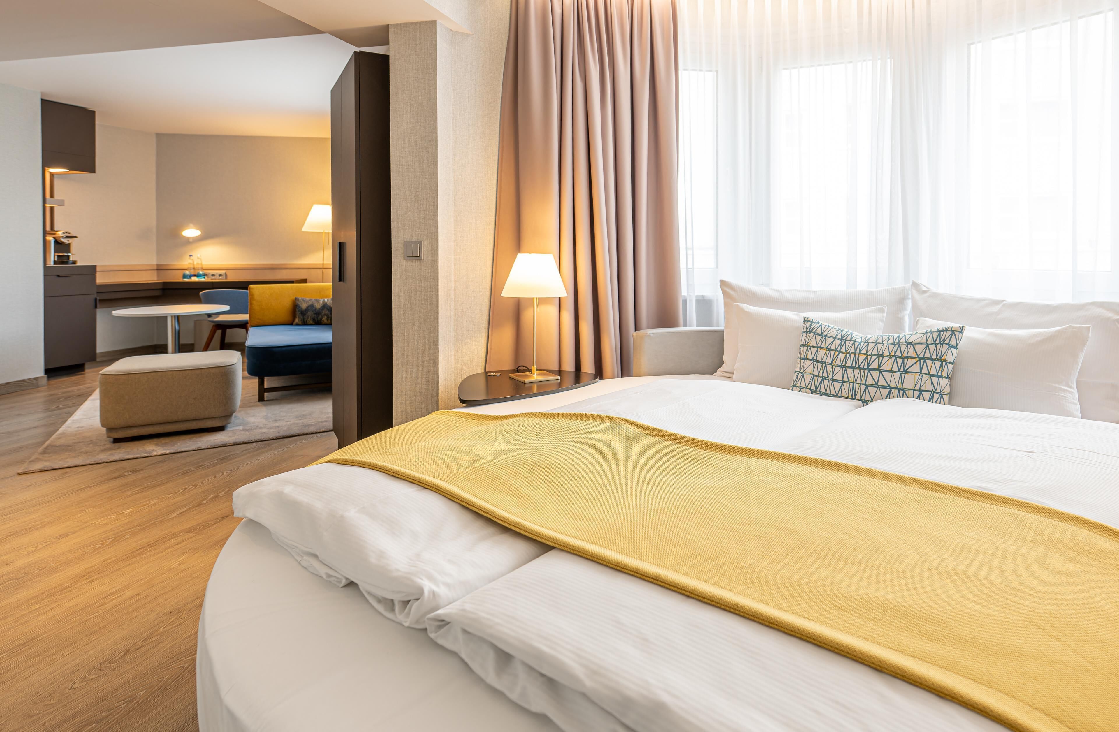 Une chambre d’hôtel avec un grand lit, un bureau, une chaise et une salle de bain visible à travers une porte ouverte.