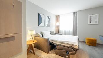 Une chambre d’hôtel moderne équipée d’un lit, d’un bureau, d’une chaise, d’une lampe et d’un petit pouf.