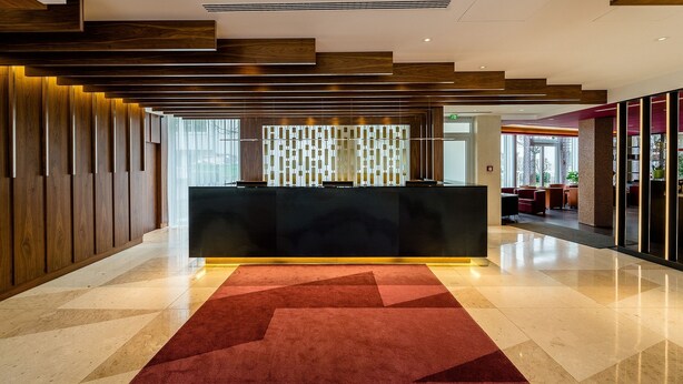 Un área de recepción moderna con un mostrador negro, paneles de madera y una pared con estampado geométrico.