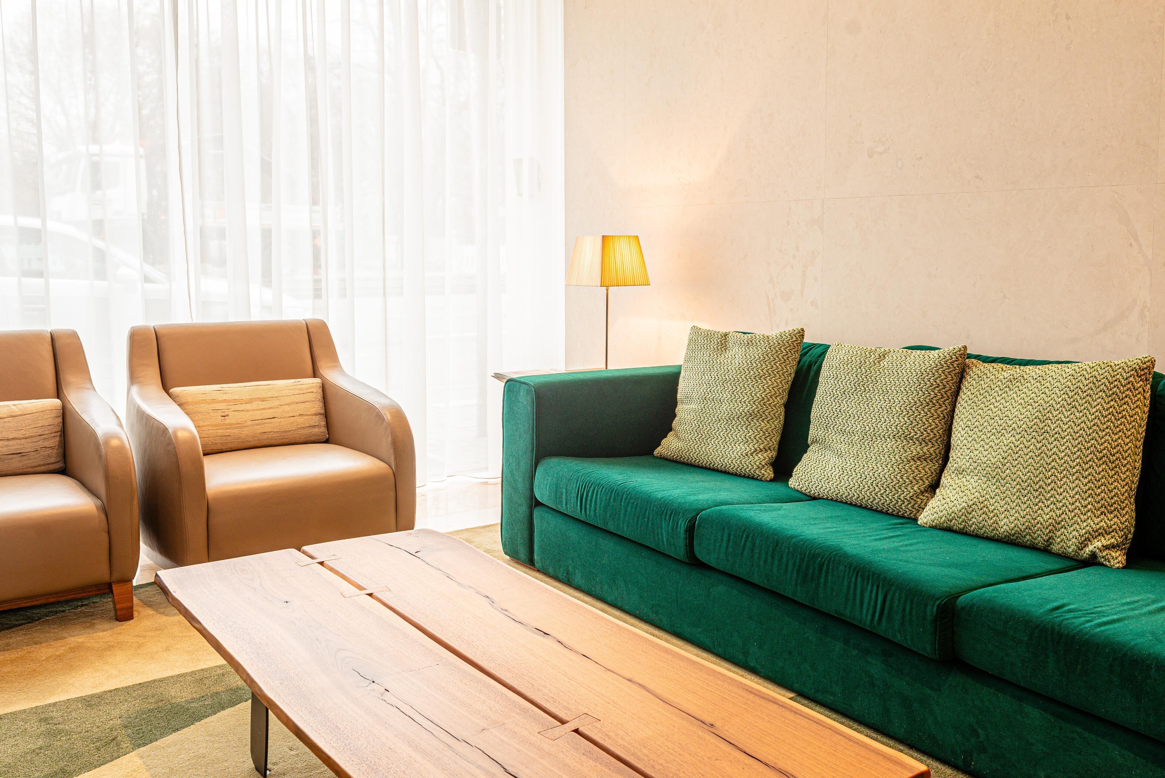 A room with a green sofa, two beige armchairs, a wooden coffee table, and a floor lamp.