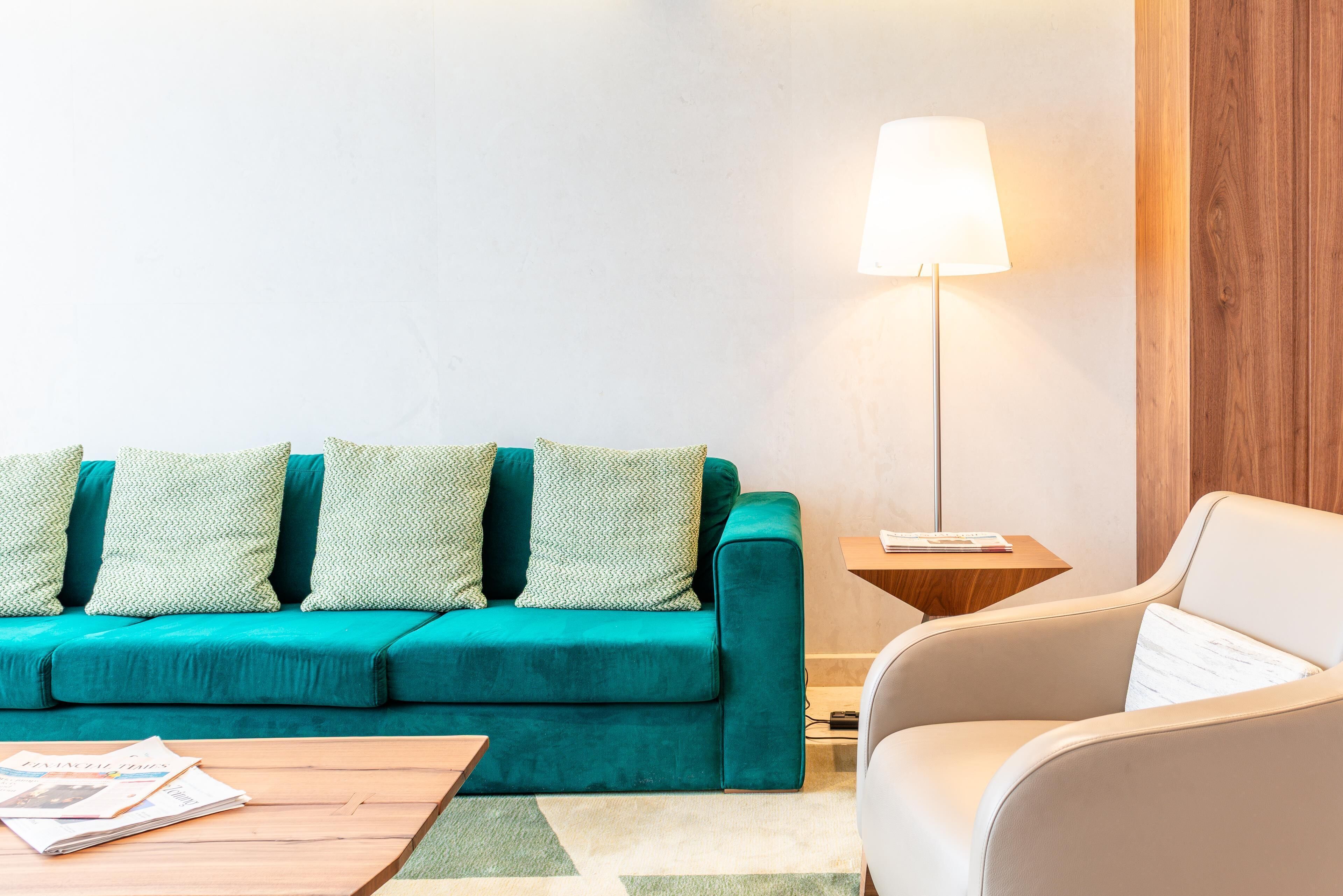 Un sofá azul verdoso con cojines estampados, un sillón blanco, una mesita de madera con una lámpara y una mesa de centro con revistas.
