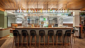 Una zona de bar con techo de madera, varios taburetes y una gran variedad de botellas y vasos en estanterías.