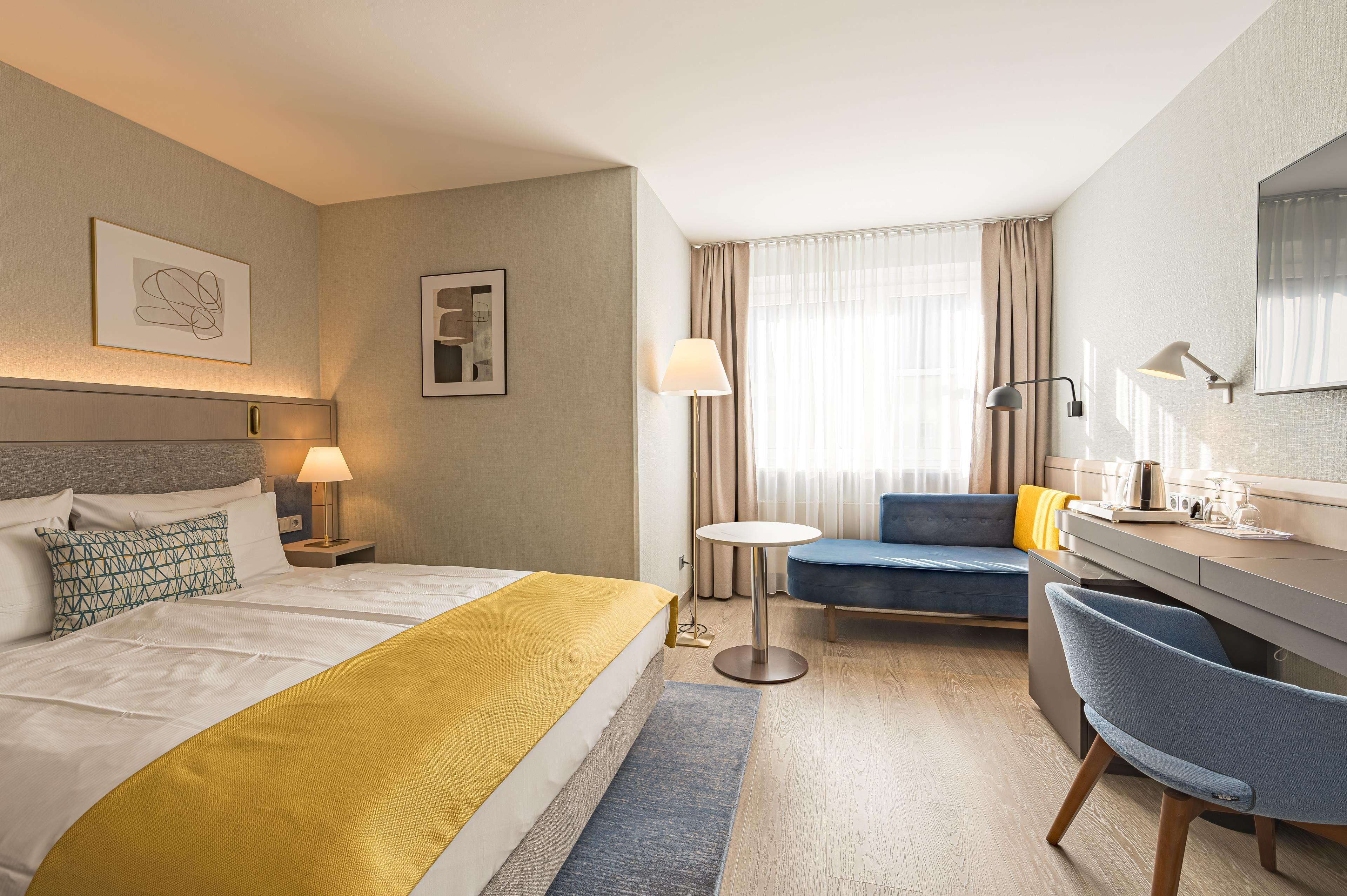 A hotel room with a bed, a desk, a chair, a round table, and a window with curtains.