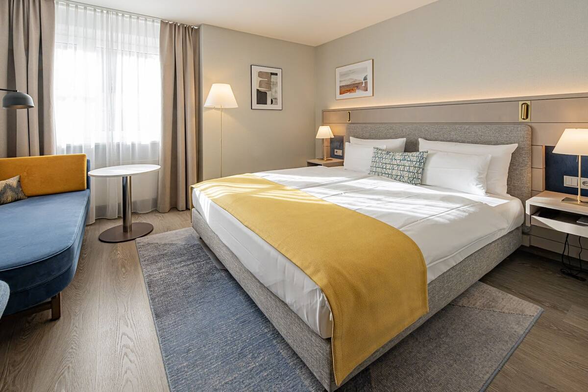 A hotel room with a bed, a sofa, two bedside tables, and a small round table.