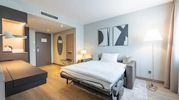 A modern hotel room with a bed, a desk, a chair, a sofa, and a lamp.