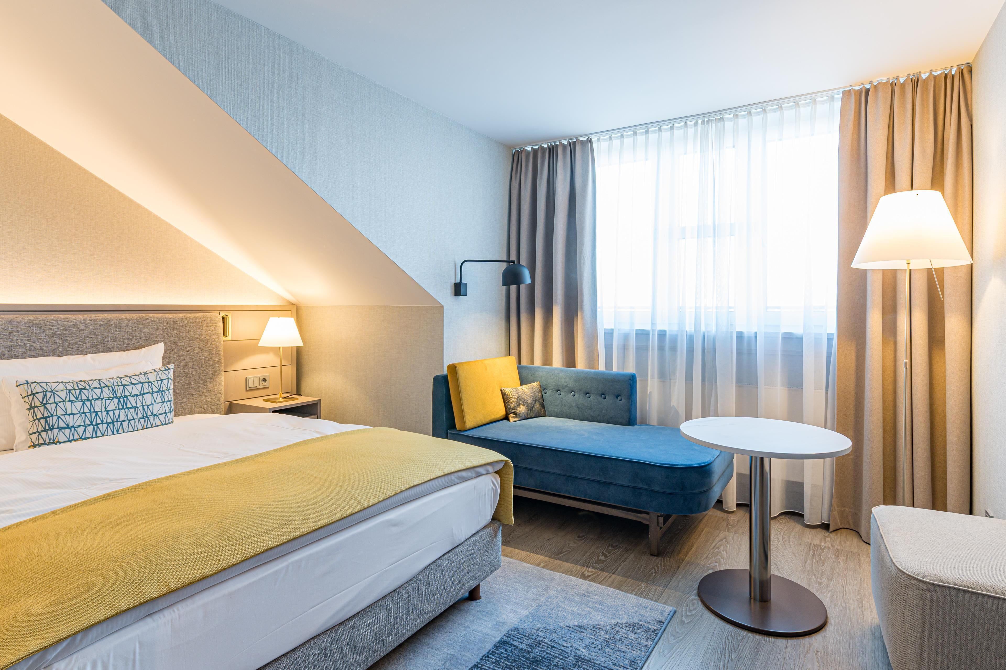 A hotel room with a bed, a sofa, a small table, and a lamp.