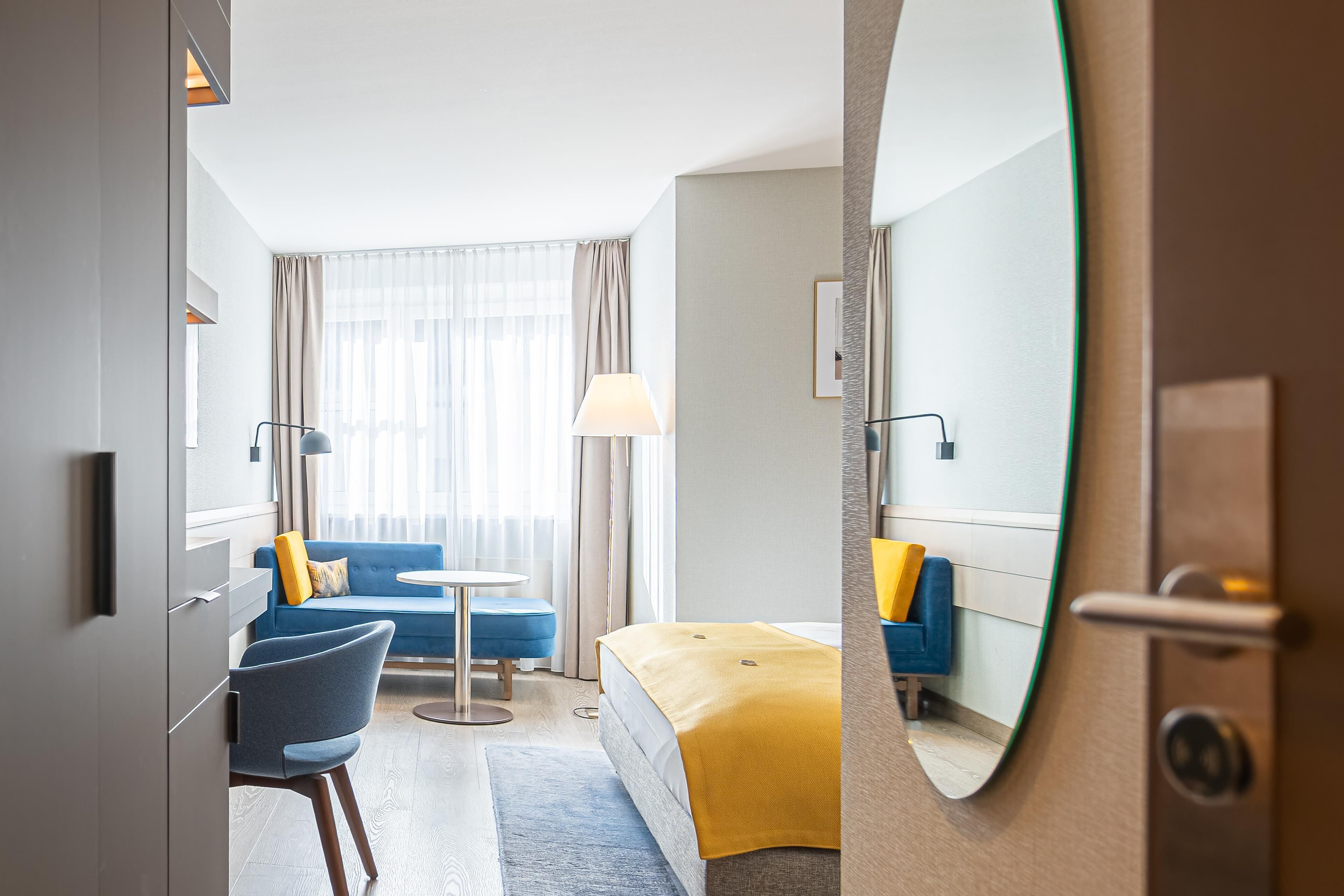 Una habitación de hotel con cama, sofá, sillón, una mesita y una lámpara.