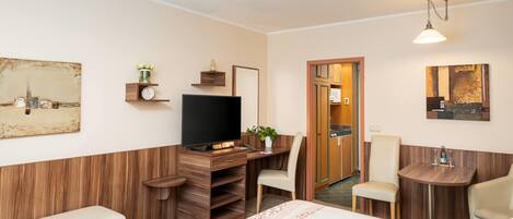 A hotel room with a bed, a desk with a computer, a chair, a small table with a bottle, and a mirror.