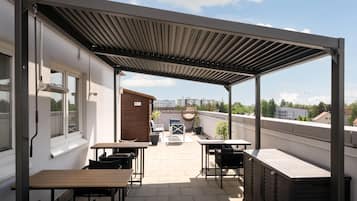 Un patio exterior techado con mesas y sillas, una silla colgante y vistas de la ciudad.