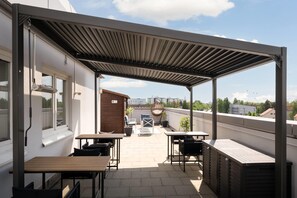Un patio exterior techado con mesas y sillas, una silla colgante y vistas de la ciudad.