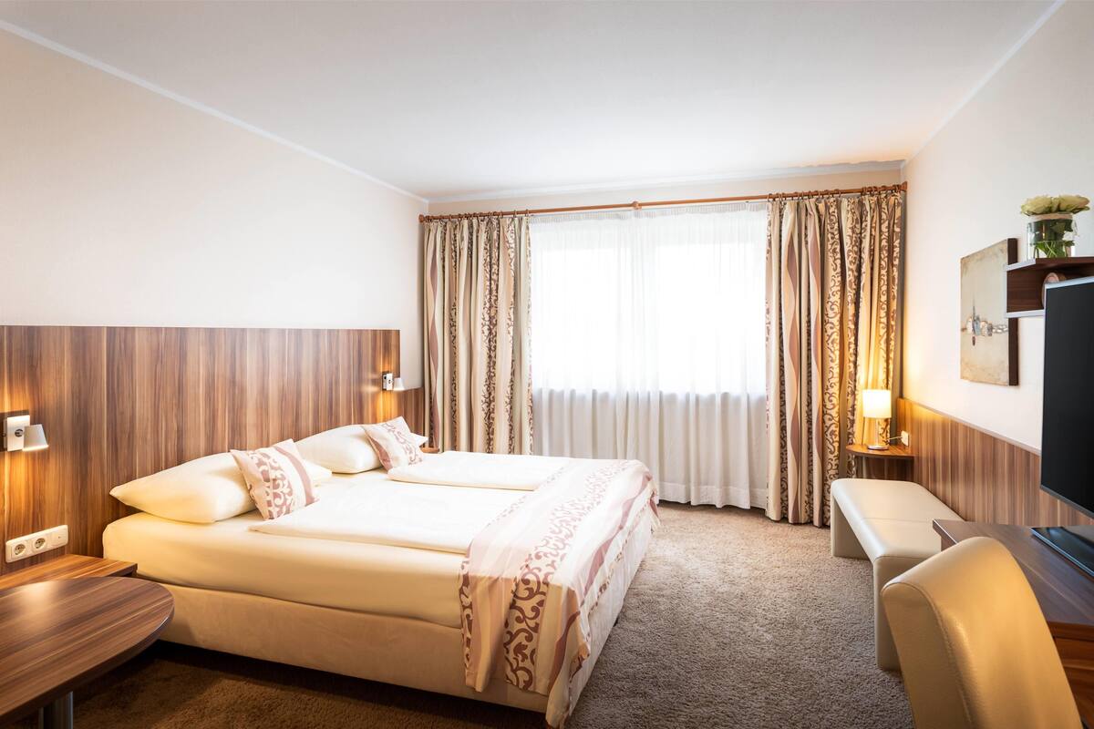 Habitación de hotel con una cama grande, un escritorio, un televisor y una ventana con cortinas.