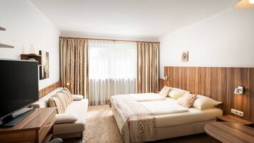Una habitación de hotel con cama, sofá, escritorio con televisor y ventana con cortinas.