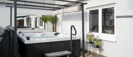 A hot tub with a pergola and steps leading to it, a palm tree, and a window with a sign.