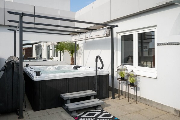 Un jacuzzi con una pérgola y escalones que lo conducen, una palmera y una ventana con un letrero.