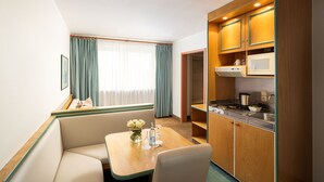 Een compacte hotelkamer met kitchenette, een eethoek met tafel en stoelen, en een zithoek met een bank.