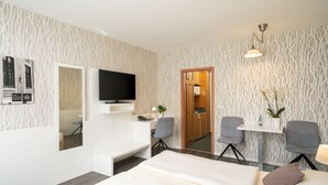 Een moderne hotelkamer met een flatscreen televisie, een bureau met stoel, een bed en een kleine tafel met een plant.