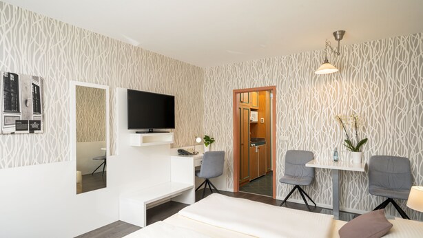 Habitación de hotel moderna con una televisión de pantalla plana, un escritorio con una silla, una cama y una pequeña mesa con una planta.