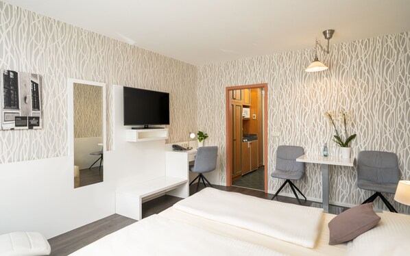 Habitación de hotel moderna con una televisión de pantalla plana, un escritorio con una silla, una cama y una pequeña mesa con una planta.