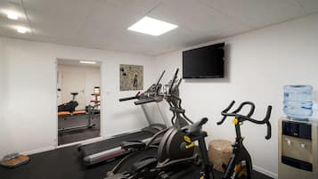 Un gimnasio con equipo de ejercicio, un dispensador de agua y un televisor en la pared.