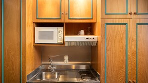 Una cocina compacta con armarios de madera, un lavamanos de acero inoxidable, un microondas y una estufa empotrada.