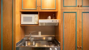 A compact kitchen with wooden cabinets, a stainless steel sink, a microwave, and a built-in stove.