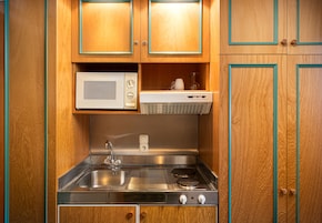 Una cocina compacta con armarios de madera, un lavamanos de acero inoxidable, un microondas y una estufa empotrada.
