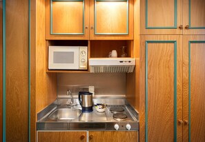 Een kleine keuken met houten kastjes, een magnetron, een waterkoker en een fornuis.