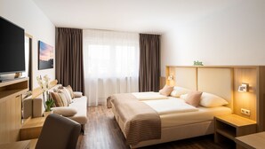 Una habitación de hotel con cama, mesitas de noche, televisión, sofá y escritorio.