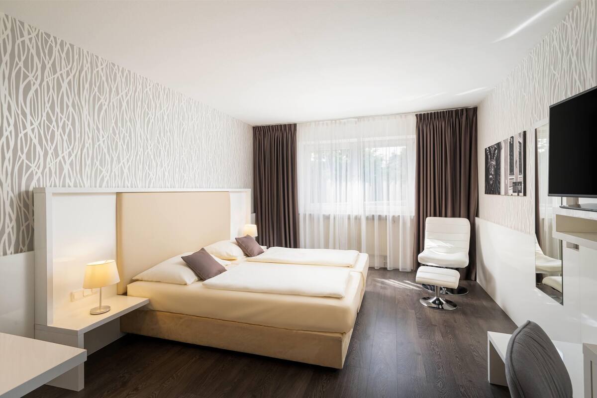 Una habitación de hotel con una cama, mesitas de noche, un escritorio, una silla y un televisor.