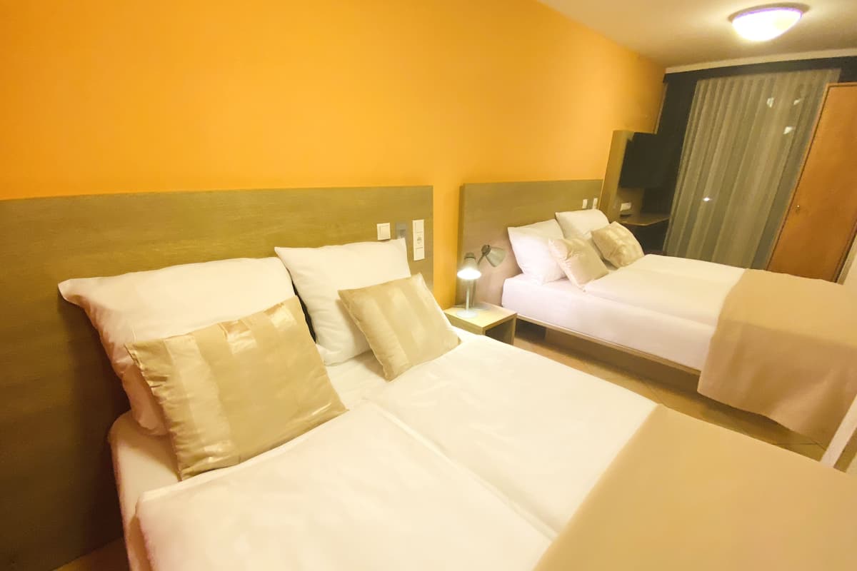 A hotel room with two beds, each with white linens and beige pillows. There is a nightstand with a lamp and a power outlet.