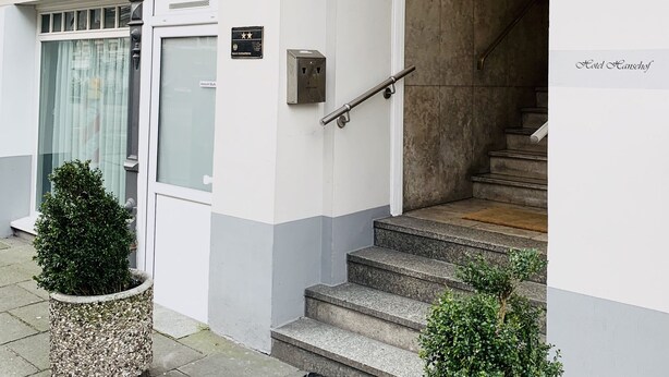 Entrada de un edificio con una escalera, una puerta con el rótulo "80/81" y una pequeña planta en maceta.