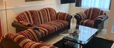 Una sala de estar con dos sofás y una mesa de centro, un televisor de pantalla plana y un gran ventanal con cortinas.
