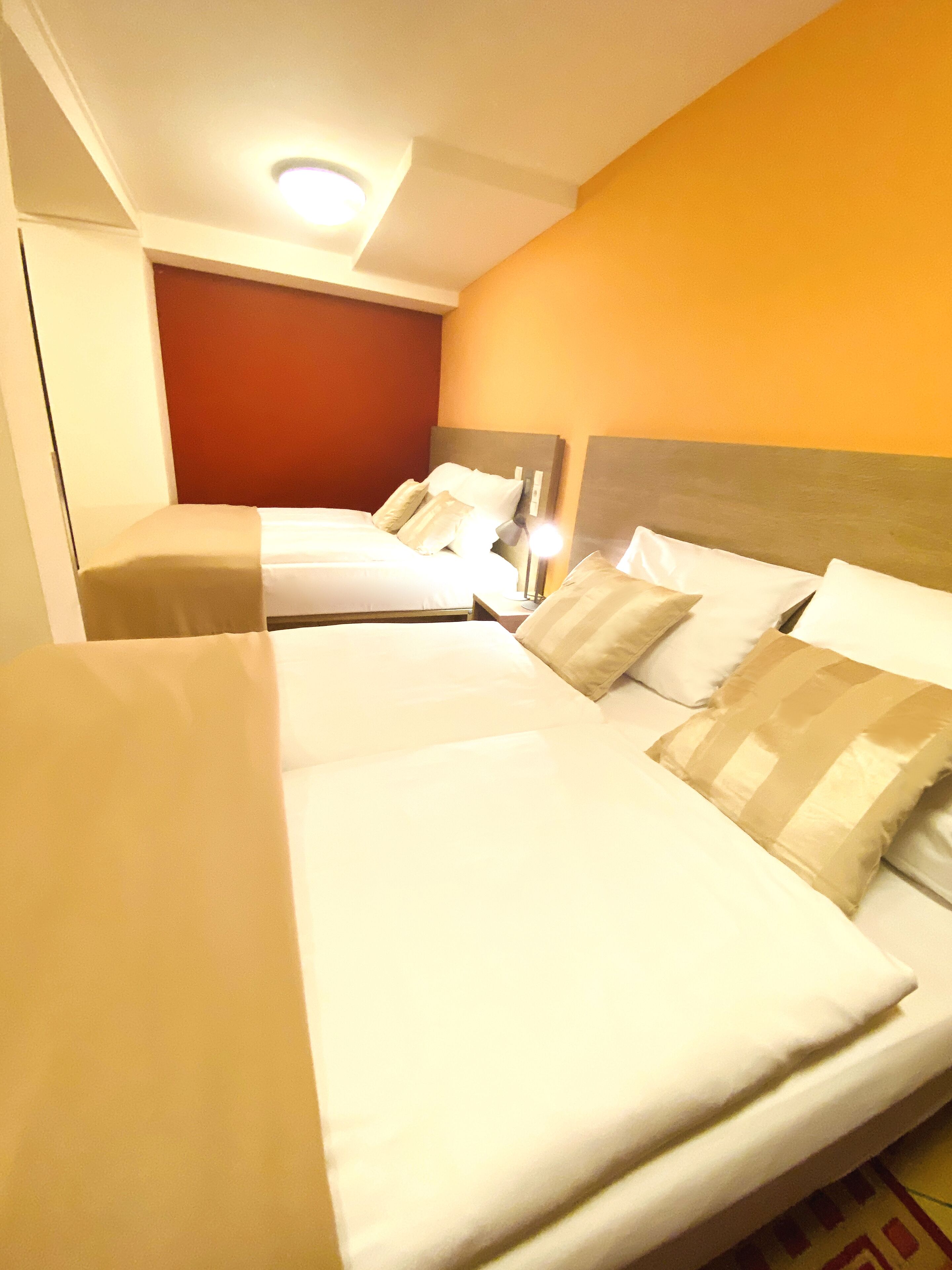 A hotel room with two beds, a red accent wall, and a ceiling light.
