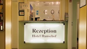 A reception desk with a sign reading "Rezeption Hotel Hansehof" in a hotel lobby.