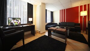 Una sala de estar moderna con un televisor de pantalla plana, un sofá negro, un sillón negro, una mesa de centro y una pared de acento roja.
