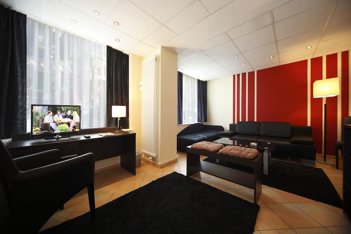 A modern living room with a flat-screen TV, a black sofa, a black armchair, a coffee table, and a red accent wall.