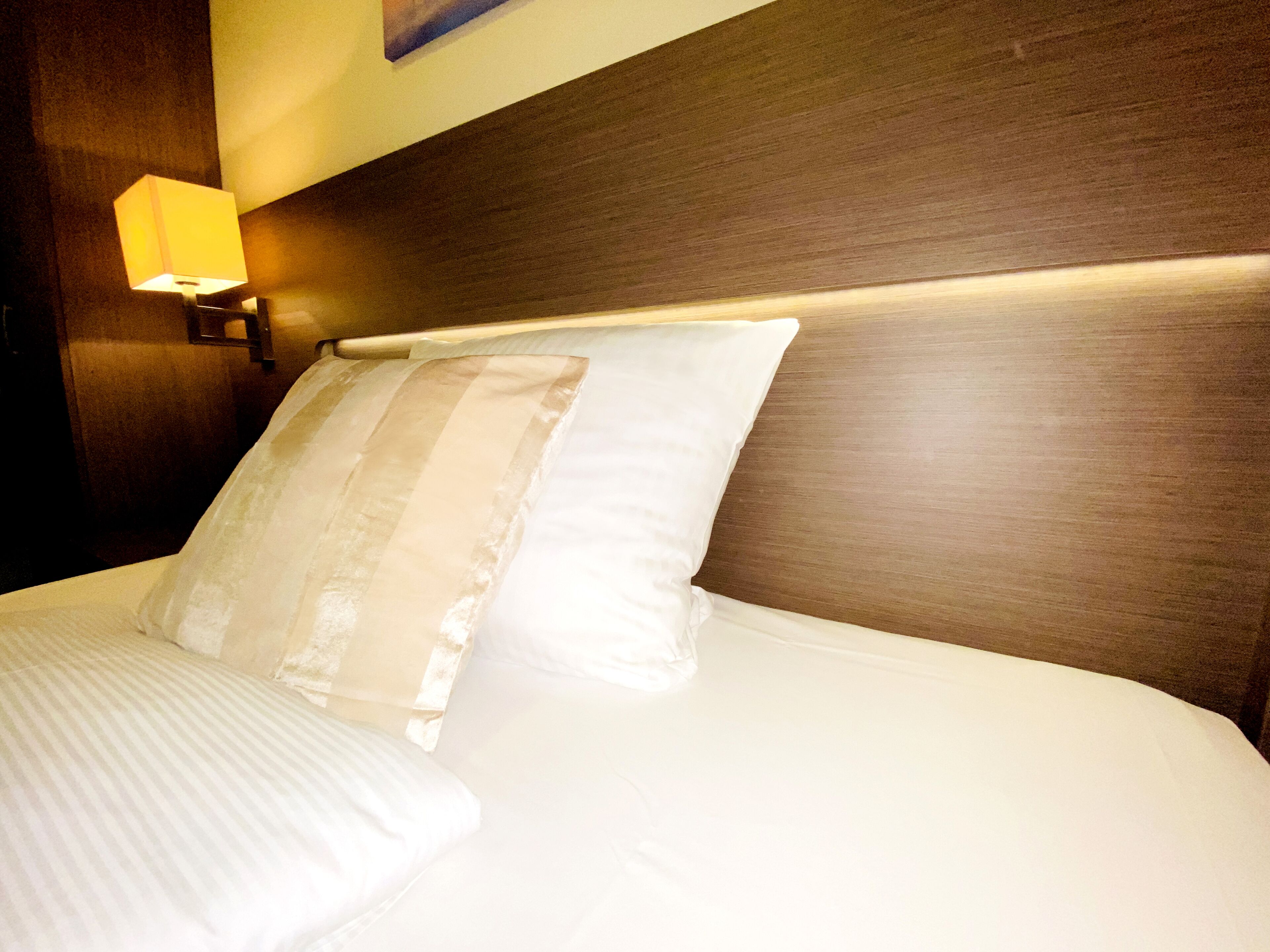 A neatly made bed with white linens and a wooden headboard.