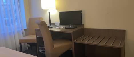 Une chambre d’hôtel avec un lit, un bureau équipé d’un ordinateur, une chaise et une lampe.